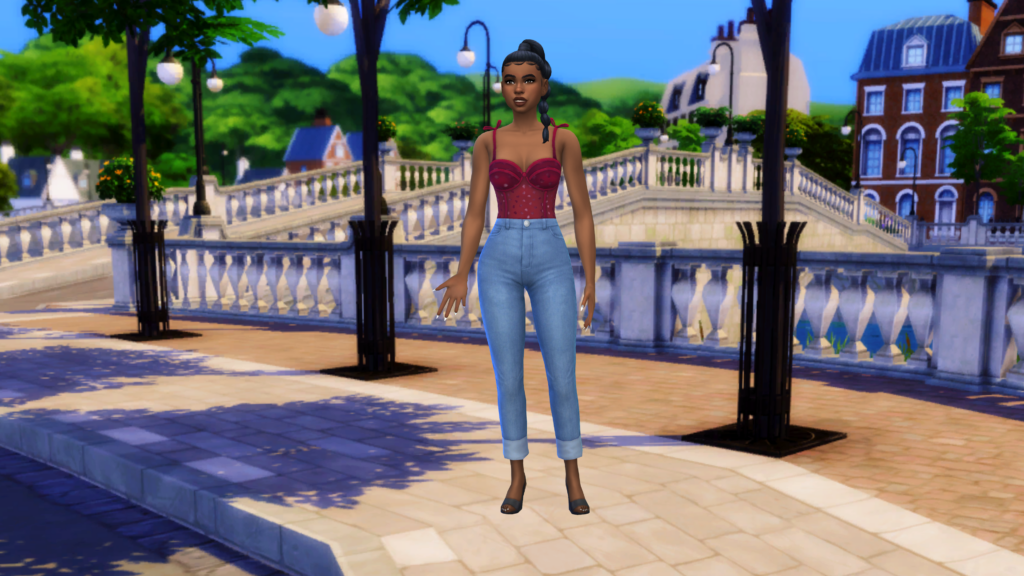 Un sim con pantalones vaqueros de cintura alta y un corsé rojo con el pelo recogido en una trenza. Este sim está parado junto a un cuerpo de agua en el mundo de Britechester en Los Sims 4