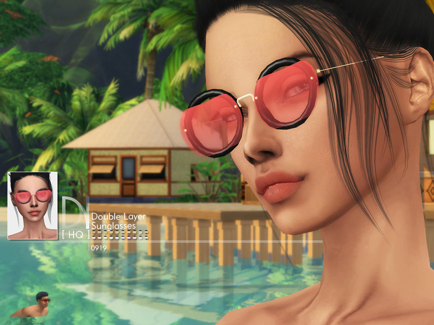 Un sim que está de pie en una playa con un paisaje tropical al fondo. Lleva puestas unas gafas de sol redondas en negro con una montura roja en la parte superior.